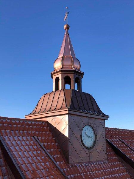 Kuppel med ur og kors på toppen af en bygning under en klar blå himmel.