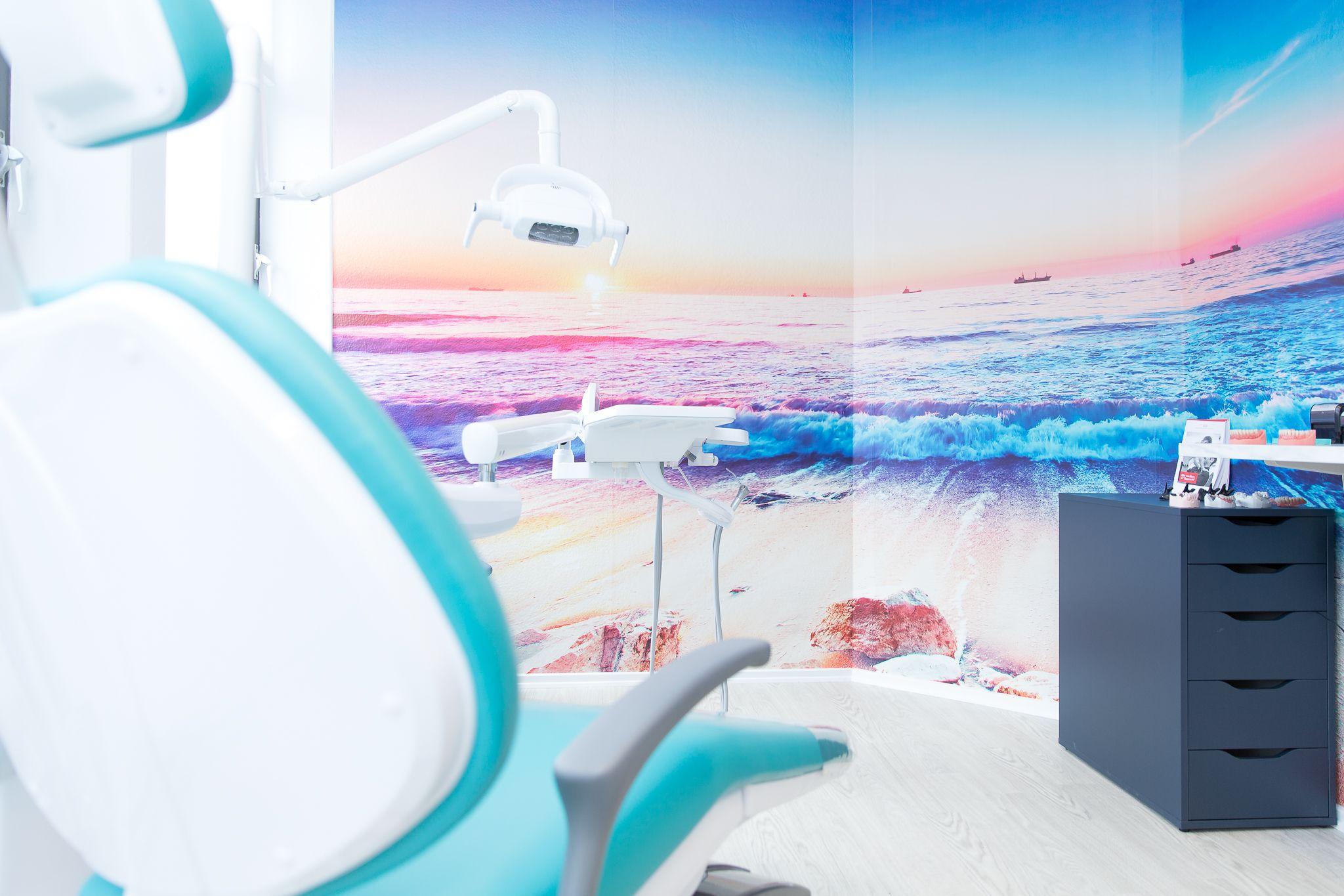 Tandlægeklinik med moderne stol og farverig vægdekoration af strand og hav.
