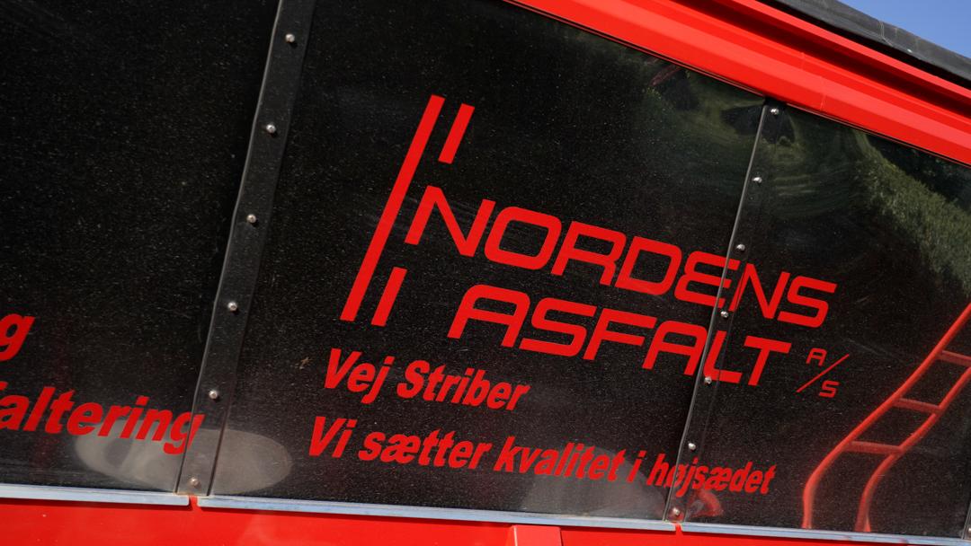 Nordens Asfalt logo på en rød lastbil med teksten "Vi sætter kraften i højbedet" og "Vej Striber".