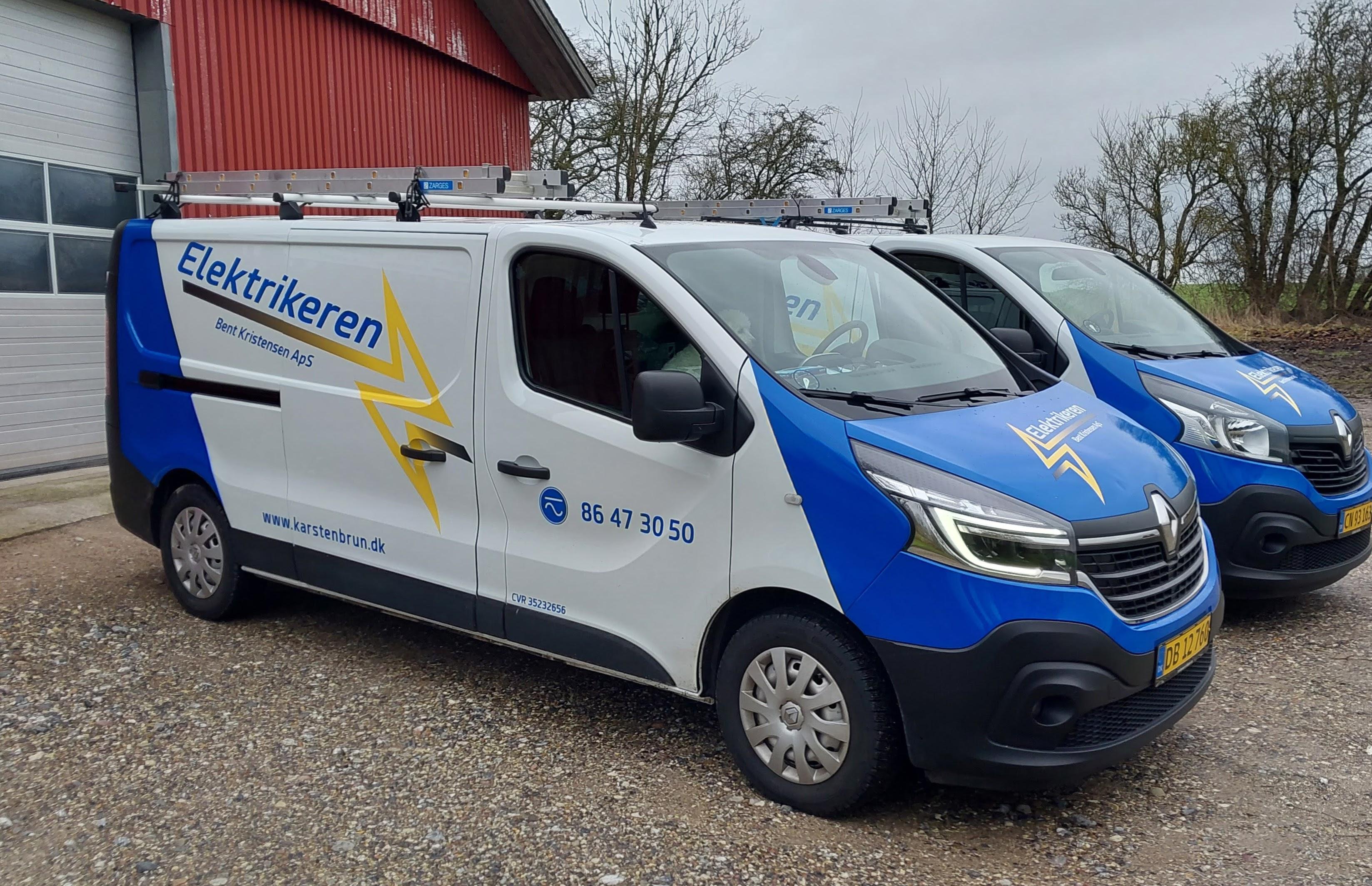 En blå og hvid varevogn med teksten "Elektrikeren" parkeret ved en bygning.