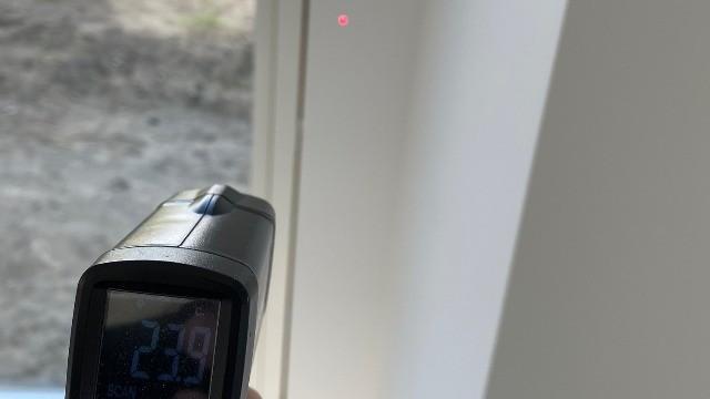 Termometer, der måler temperaturen på en væg, med en rød laserprik synlig i baggrunden.