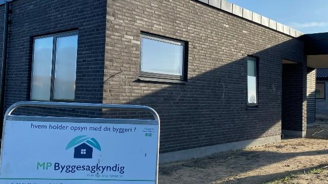 Nybygget hus med mørk murstensfacade og vinduer, samt skilt for MP Byggesagkyndig i forgrunden.
