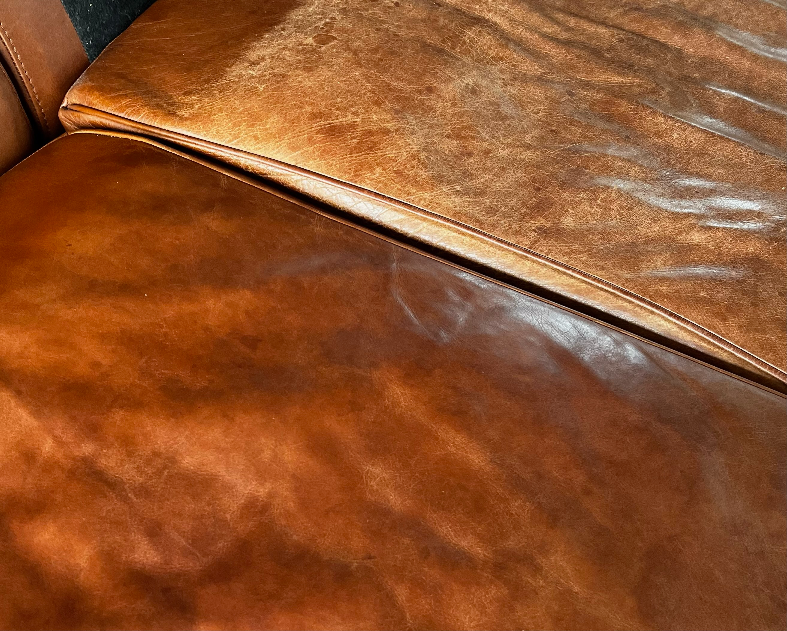 Lædersofa med to forskellige nuancer af brunt læder, der viser slid og patina.