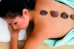 Kvinde får en hot stone massage med glatte sten placeret på ryggen, indpakket i et håndklæde.