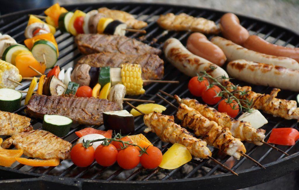 Grillmad med grøntsager, kødspyd, pølser og majs på en grillrist, klar til servering.
