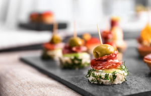 Lækre tapas med skiver af salami, oliven og friske krydderurter præsenteret på en sort skiferplade.