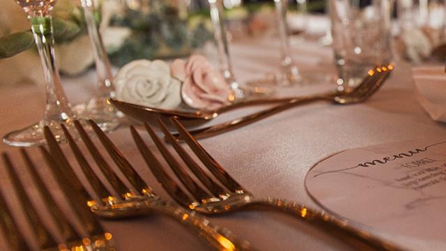 Elegant borddækning med guldbestik, glas og blomsterdekorationer til en festlig lejlighed.