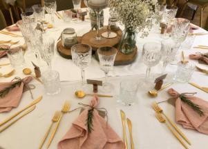 Elegant dækket bord med glas, guldbestik og lyserøde servietter pyntet med rosmarin.