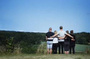 Fem personer står sammen og kigger ud over en grøn dal under en blå himmel.