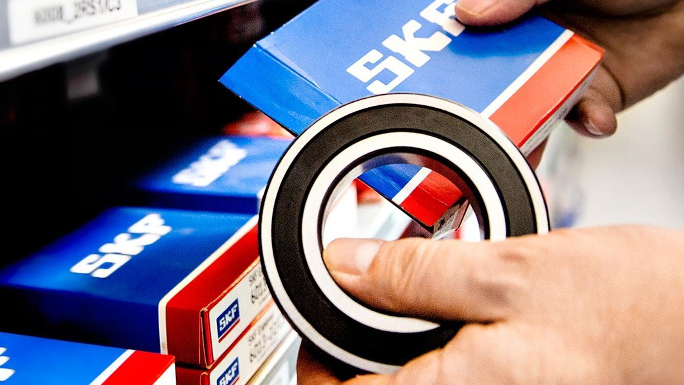 Hånd der holder en sort og hvid leje fra SKF, mens den vælger en pakke fra hylden.