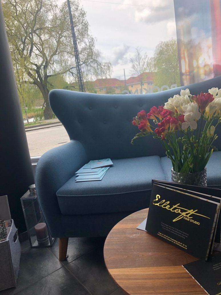 En blå sofa med blomster og en menu på et bord i en hyggelig café med udsigt til en park.