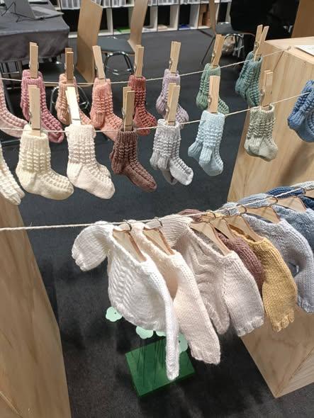 Håndstrikkede sokker og en trøje hængende på snor med tøjklemmer i en butik.