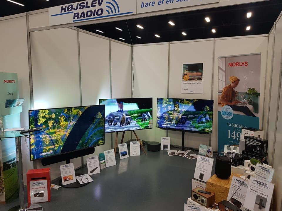 Udstilling med flere fladskærms-tv'er og elektroniske apparater i en messehal for Højslev Radio.