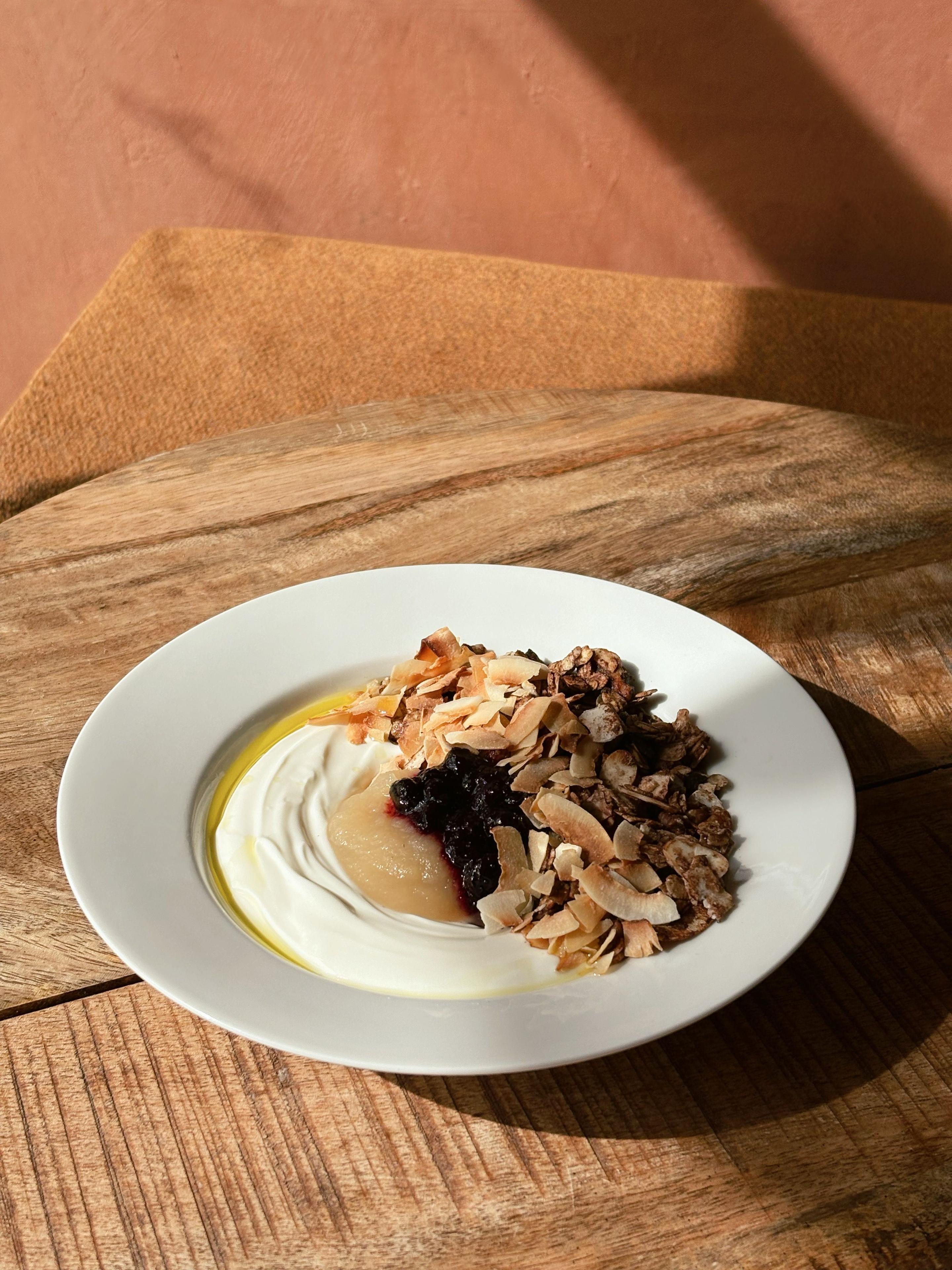 En tallerken med granola, græsk yoghurt, honning og bær på et træbord.