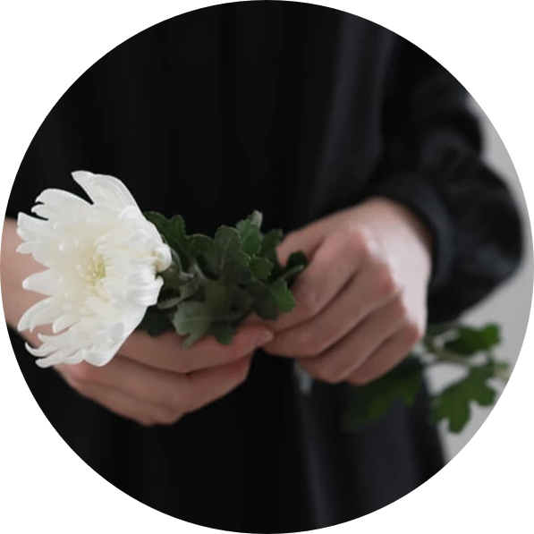 En person holder en hvid blomst med grønne blade i hænderne, iført en sort bluse.