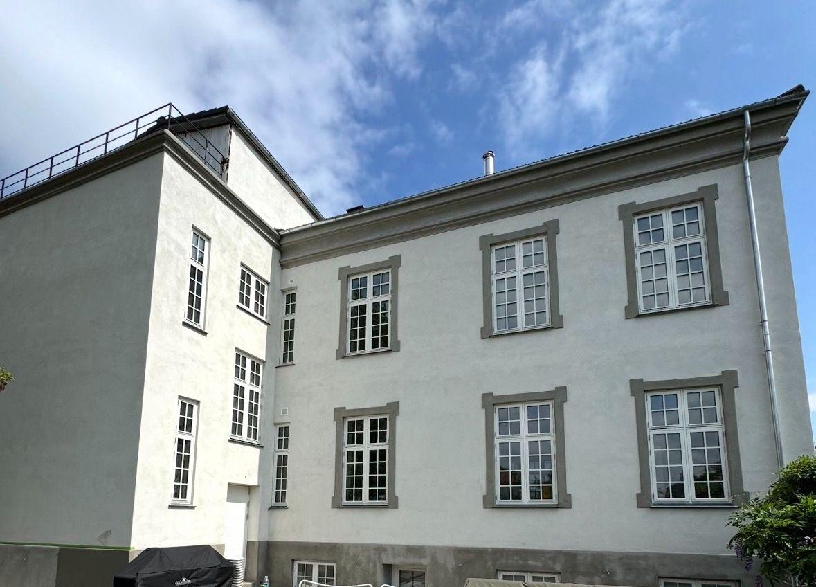 Et hvidt hus med mange vinduer og en blå himmel i baggrunden.