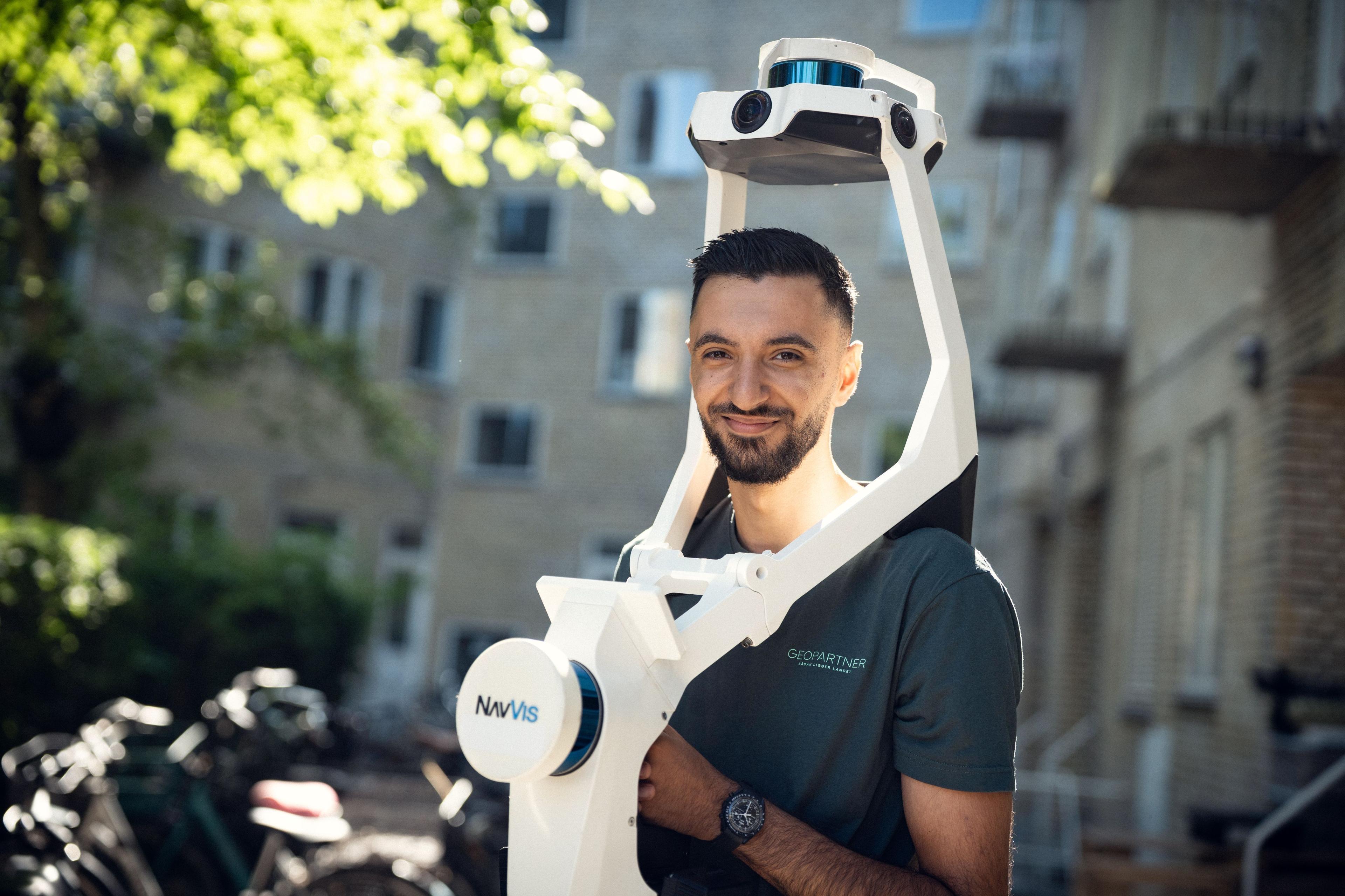 Mand med en avanceret 3D-scanner, der står udendørs ved bygninger og cykler.