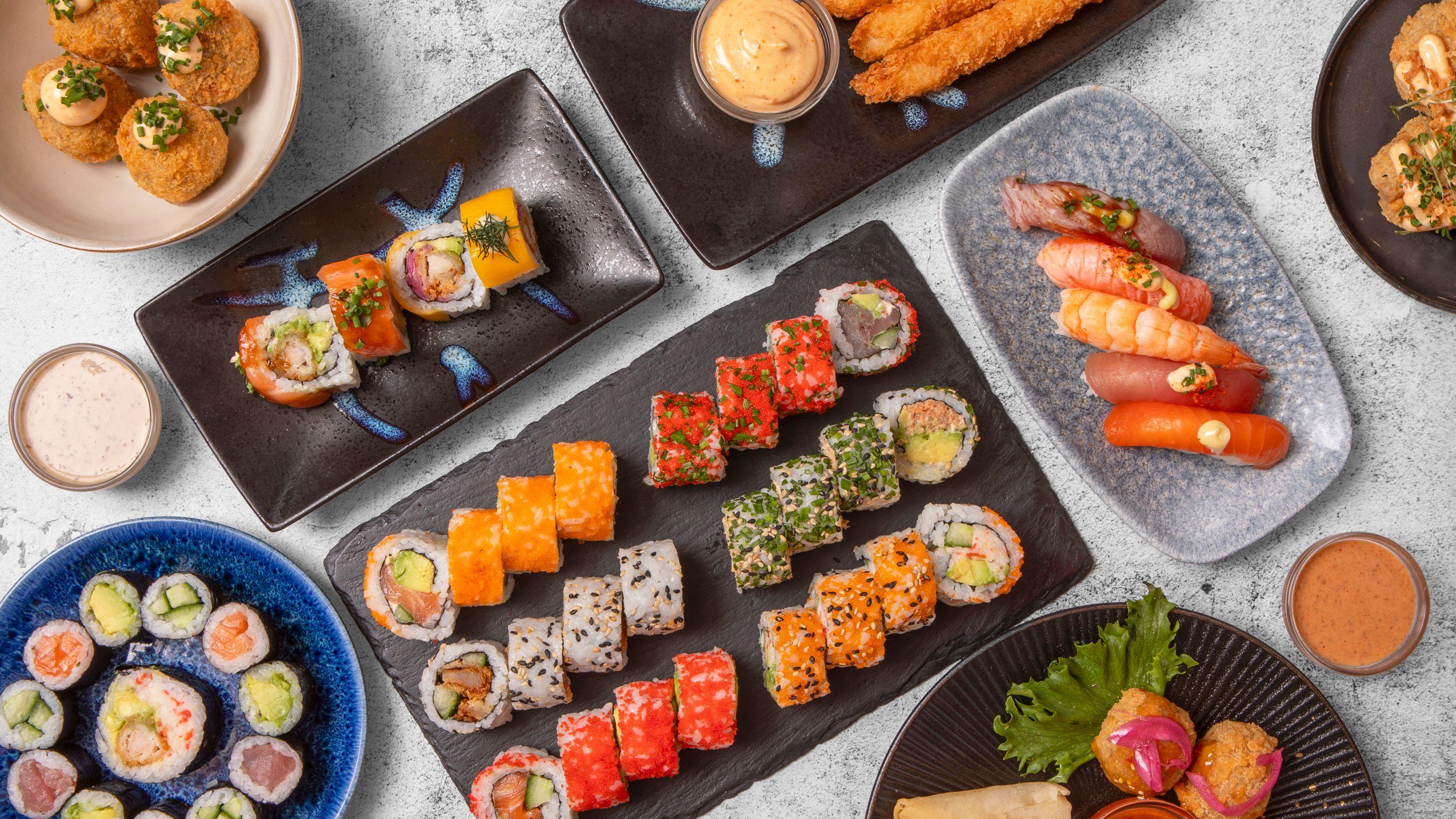 Et udvalg af farverigt sushi og japanske retter præsenteret på sorte og blå tallerkener.