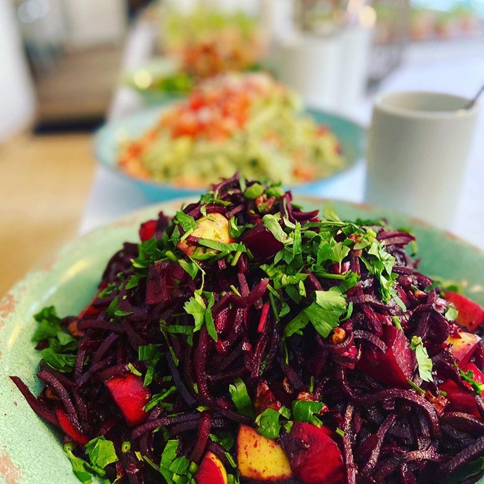 Farverig rødbedesalat med æbler og friske krydderurter i forgrunden, med salater i baggrunden.