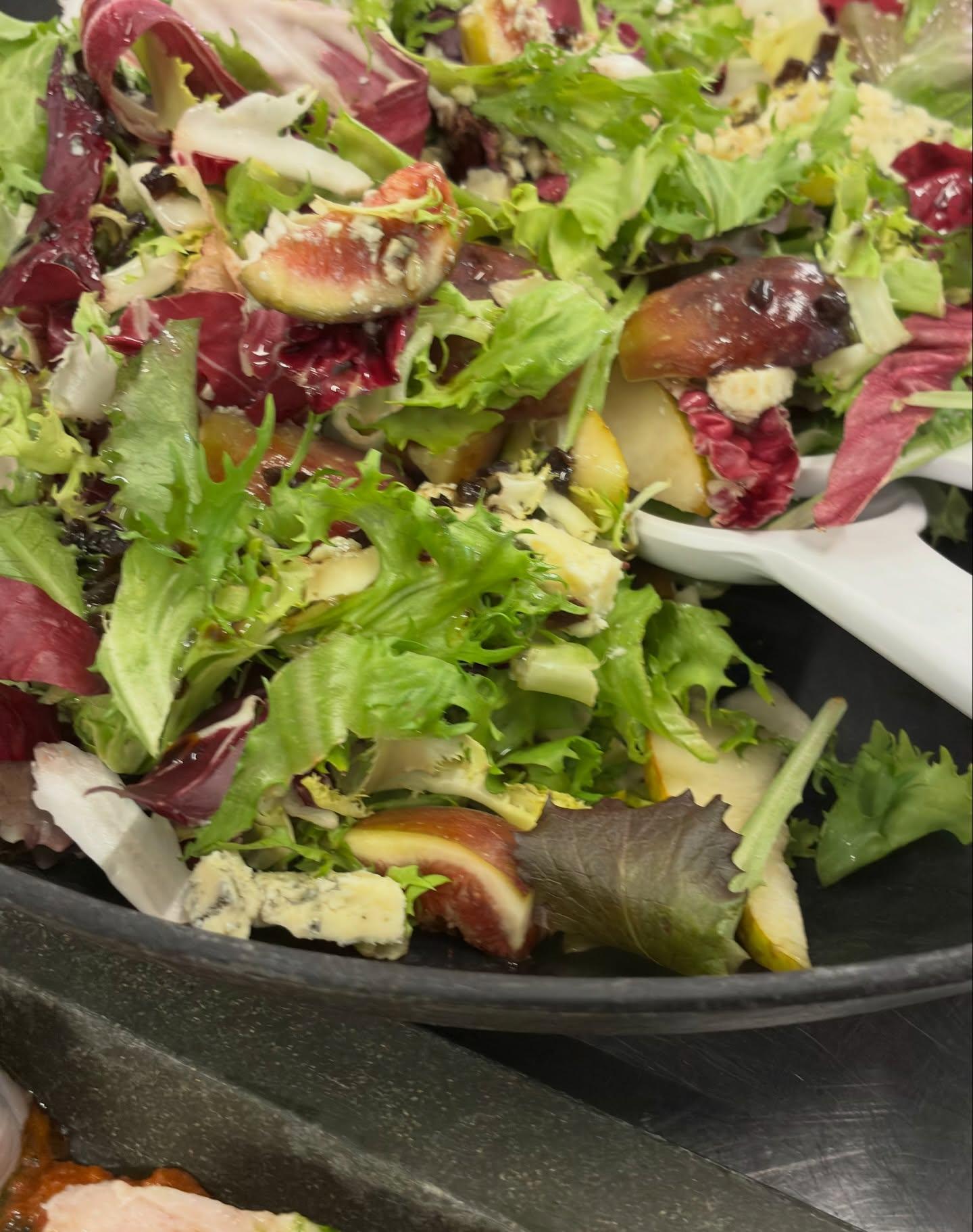 Farverig salat med blandede grøntsager, herunder salatblade, radicchio og frugtstykker.