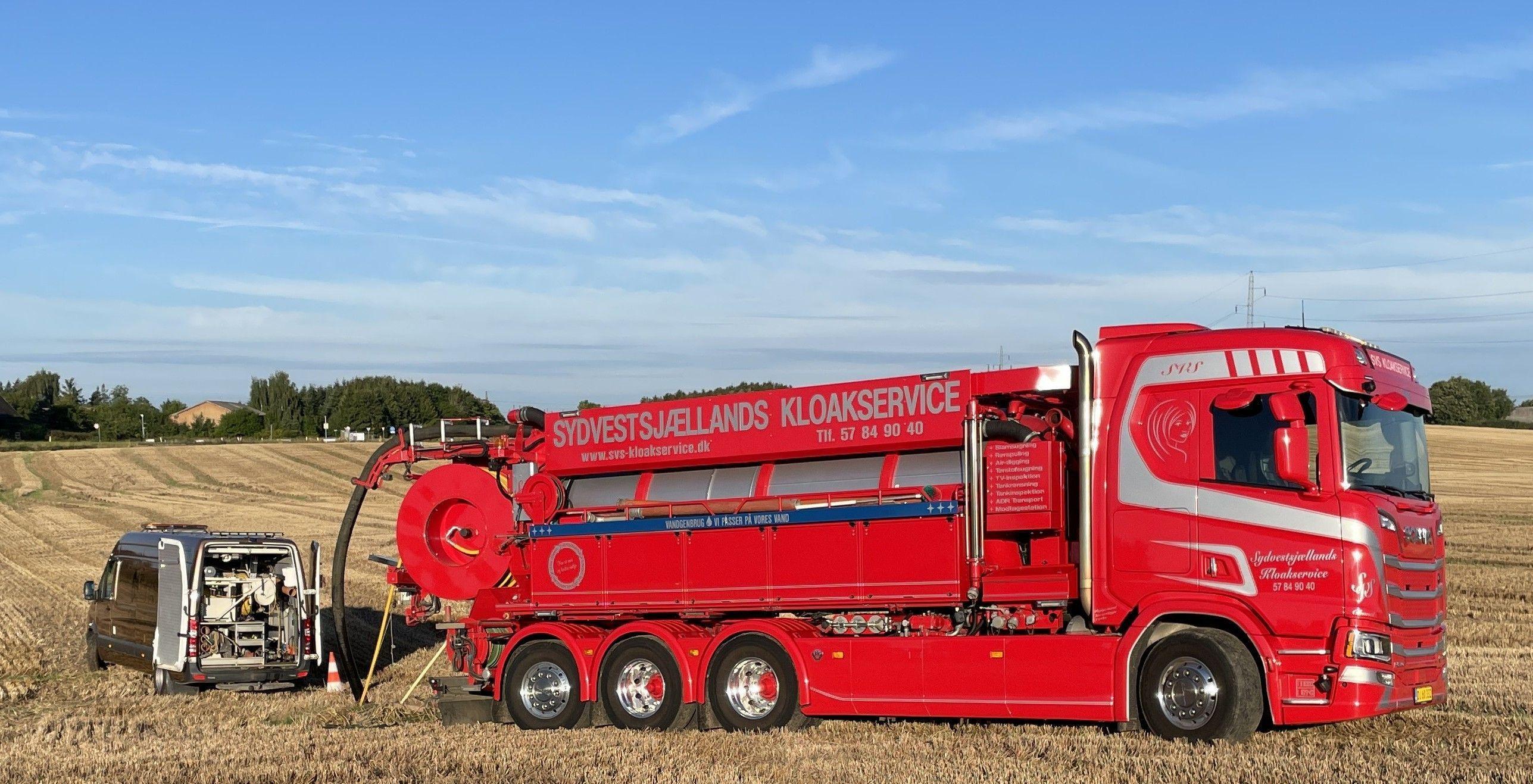 Rød lastbil med sugemaskine arbejder på en mark under en blå himmel.