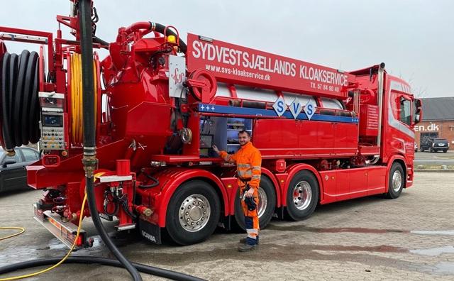 En rød kloakbil fra Sydvestsjællands Kloakservice med en medarbejder i arbejdstøj ved siden af.