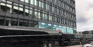 To store med moderne glasfacade og to sorte busser parkeret foran.