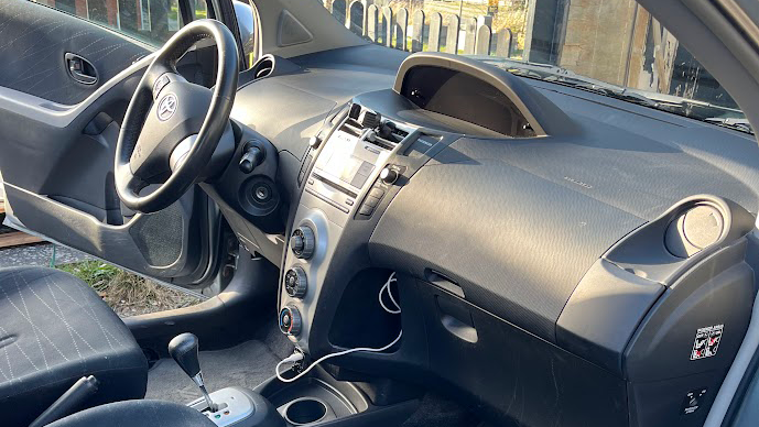 Billede af interiøret i en bil med sort dashboard, rat og gearstang, samt en skærm i midten.