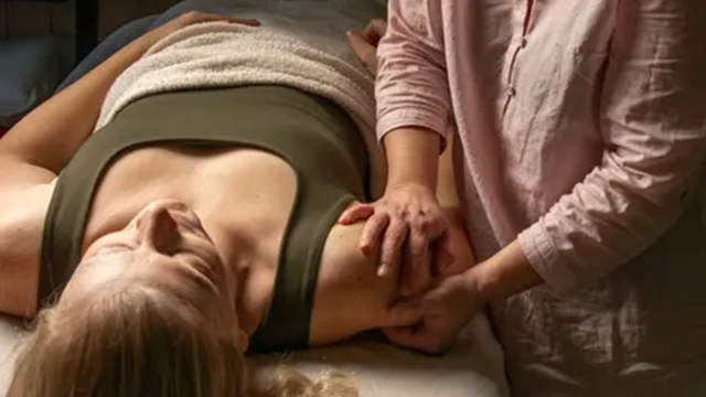 En kvinde får massage på en briks, mens en behandler arbejder på hendes arm.