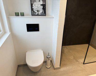 Moderne badeværelse med toilet, glasbruser og kunstværk på væggen.