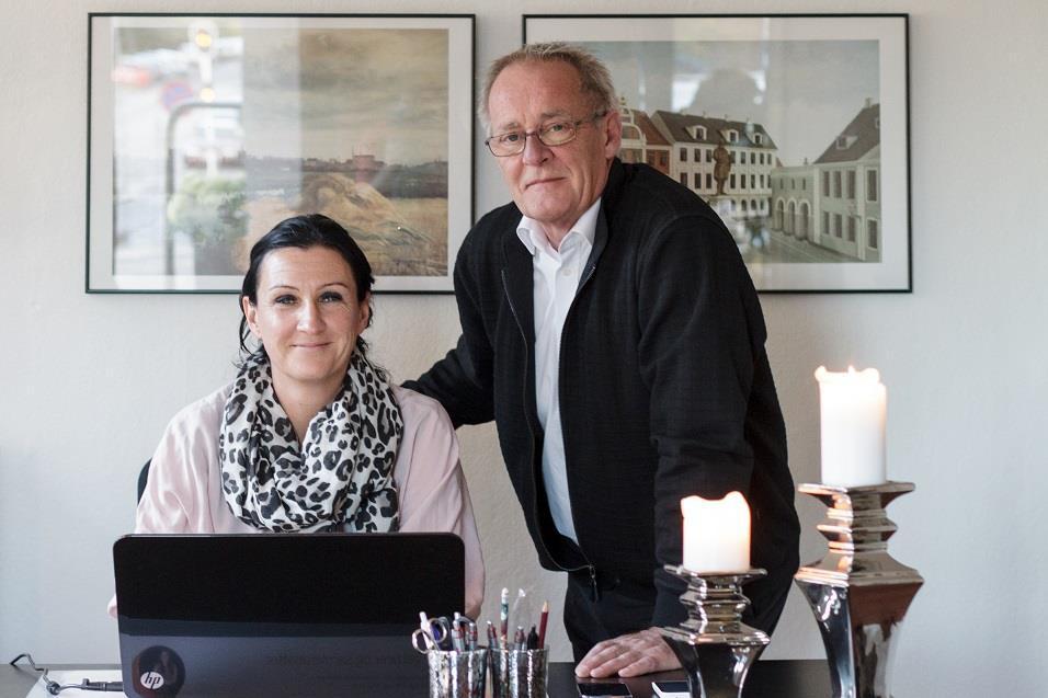 To personer står ved et skrivebord, en kvinde med sort-hvidt tørklæde og en mand i sort jakke, med lys og dekorationer.