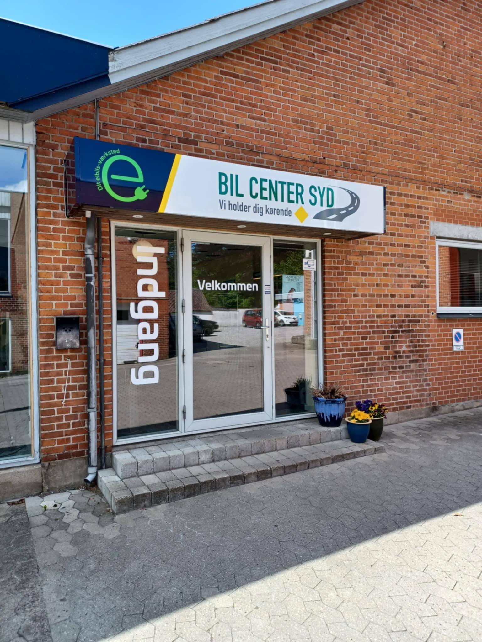 Indgangen til Bil Center Syd med en velkomstskilt og blomsterkasser foran bygningen.