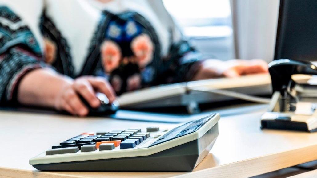 En person arbejder ved et skrivebord med en computer og en lommeregner i forgrunden.