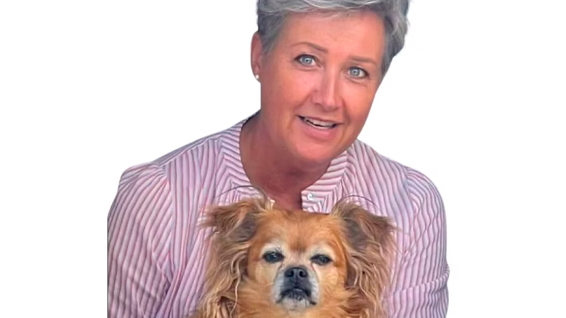 En kvinde med kort gråt hår holder en lille hund i sine arme og smiler til kameraet.