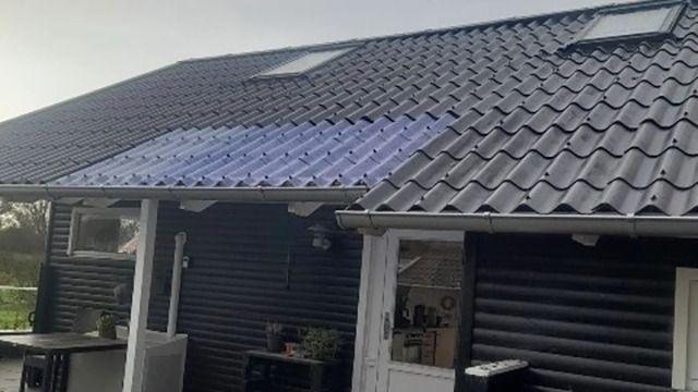 Et hus med sort tag og solpaneler, der er installeret på taget, med vinduer og en terrasse i forgrunden.