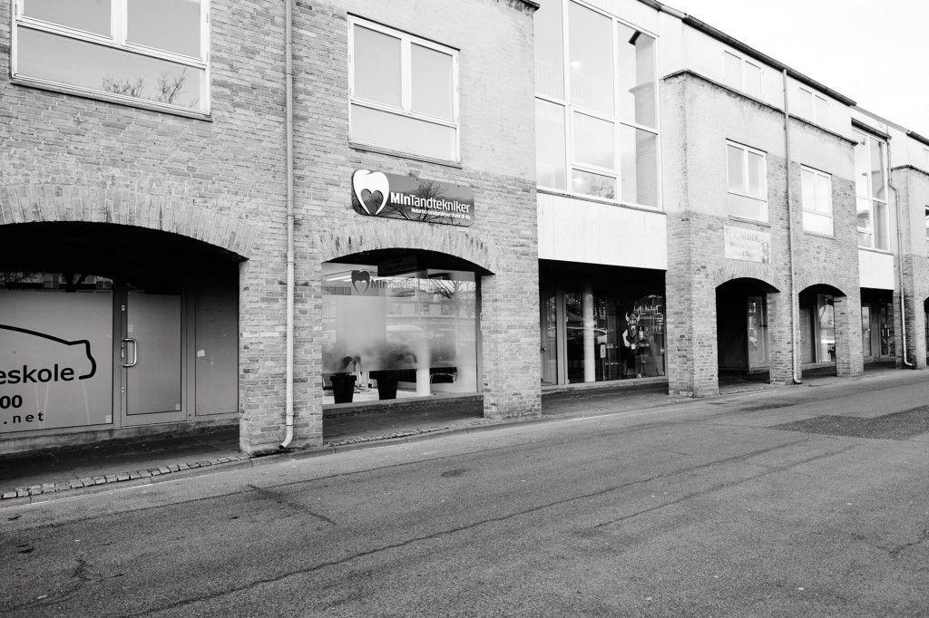 Facade af en bygning med butikker og en tandlægeklinik i en bygade.