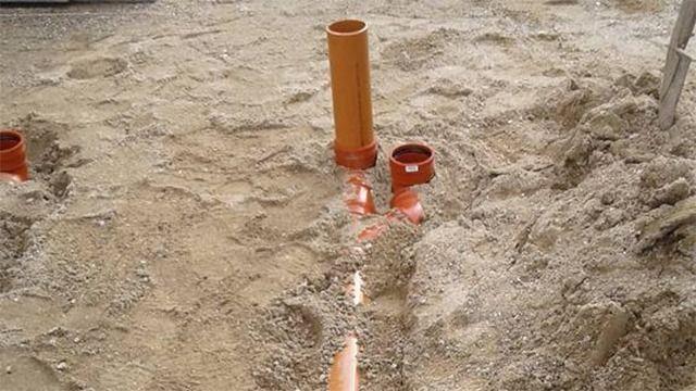 Orange rør og sand på byggeplads, der viser installation af kloaksystem.