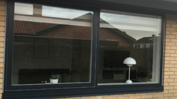 Vindue i sort ramme med udsigt til hus og lampe indendørs.