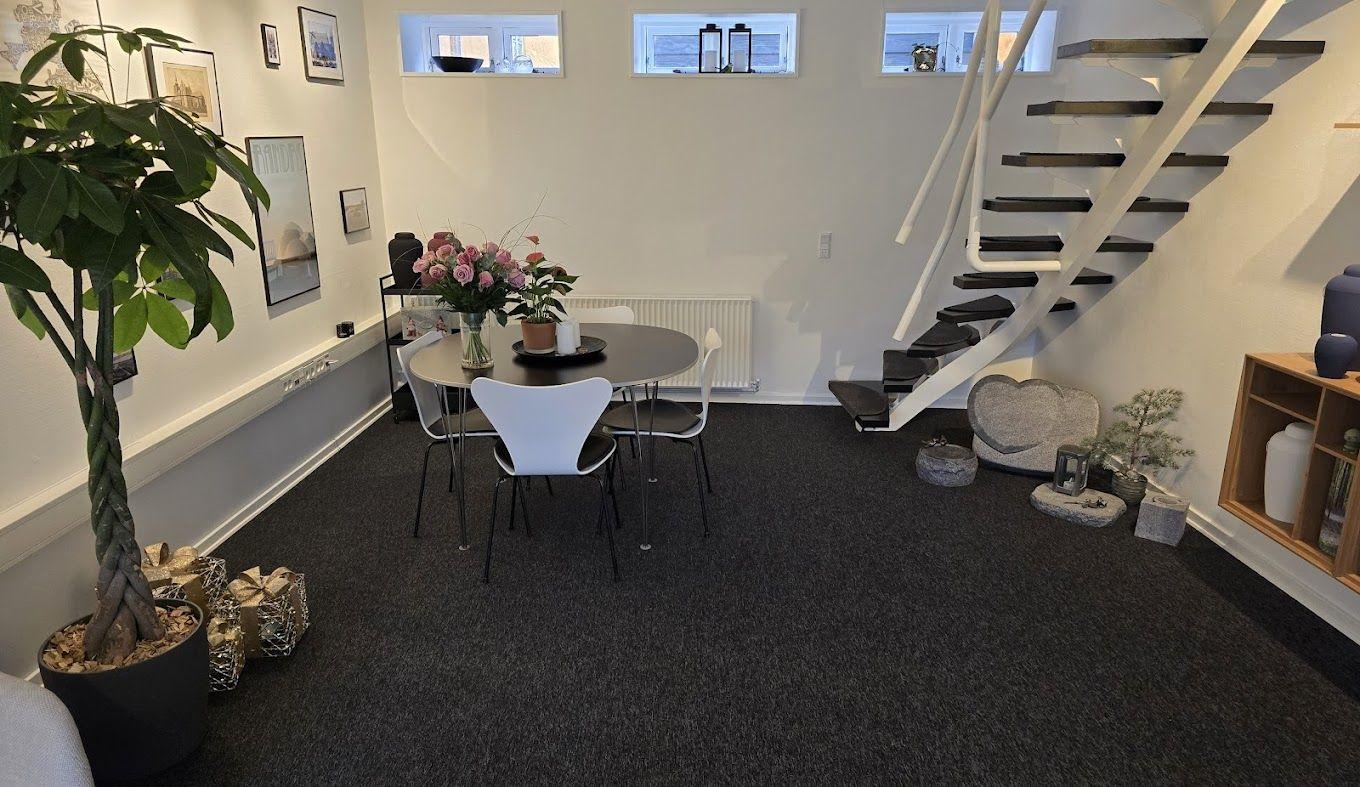 Moderne stue med spisebord, stole, planter og en trappe i en lys indretning.