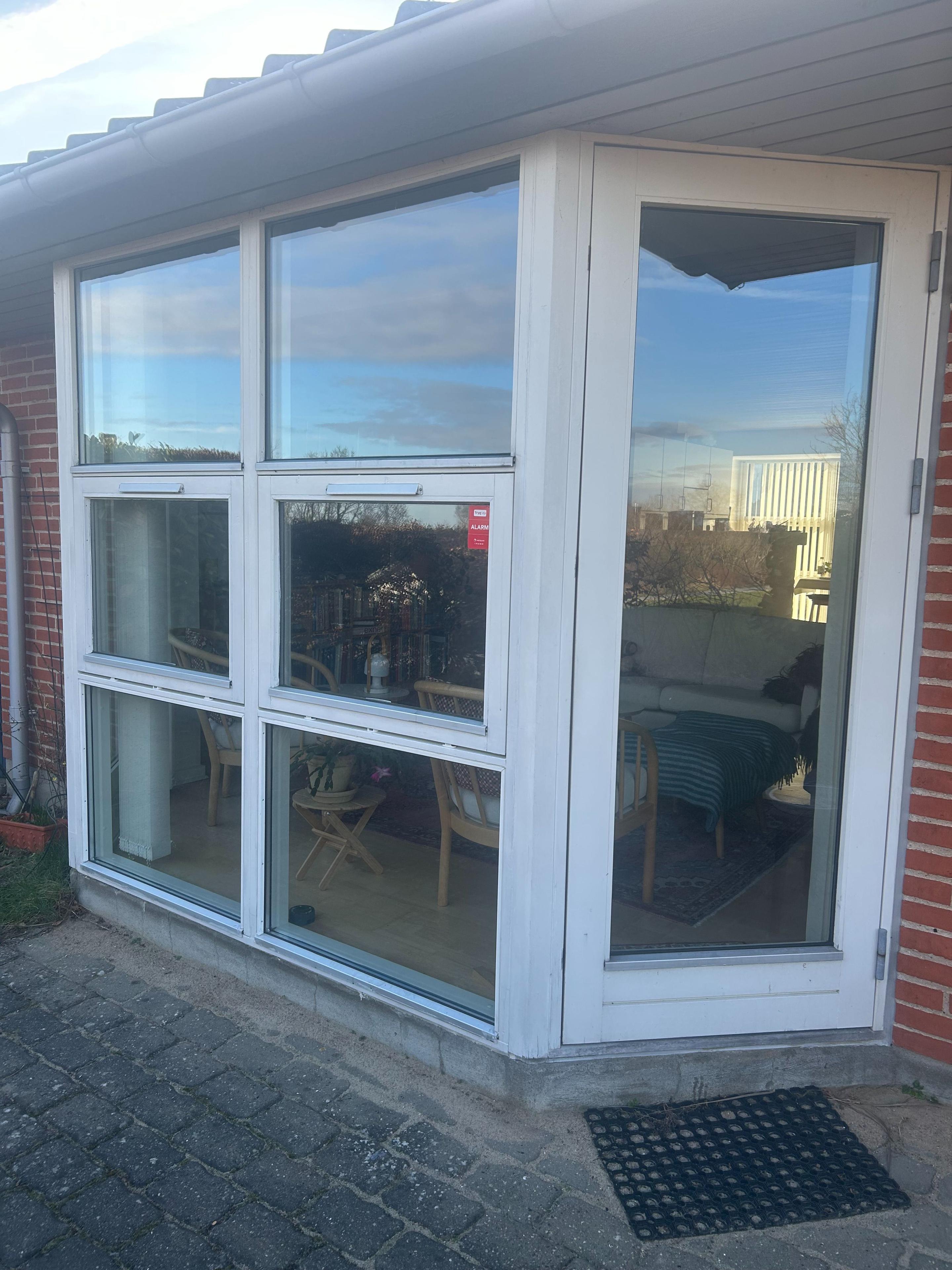 En moderne hvid terrassedør med store vinduer, der giver udsigt til en indendørs spisestue.