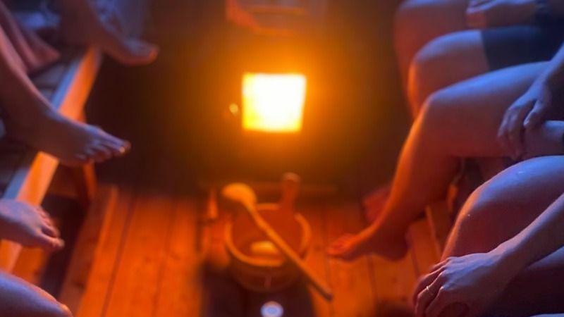Fødderne på personer, der sidder i en sauna, med en varm ovn i midten og et træredskab ved siden af.
