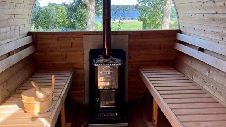Indvendig udsigt af en sauna med træbænke og en brændeovn i midten, omgivet af natur.