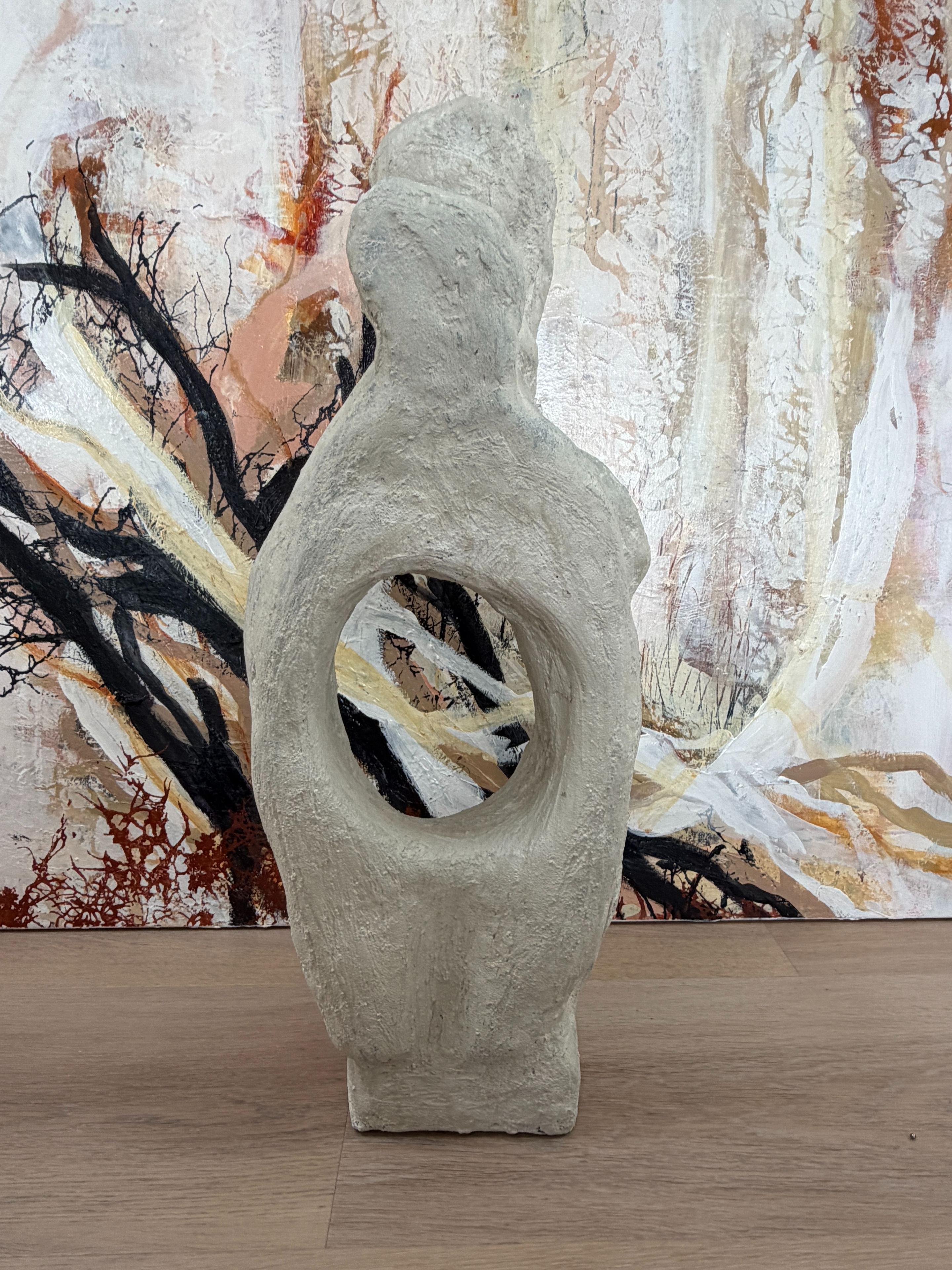 En skulptur i lys sten med et hul i midten, placeret foran en farverig abstrakt baggrund.