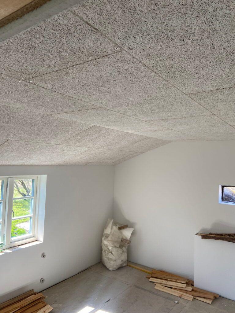 Indvendig udsigt af et værelse med gråt loft, vinduer og byggeaffald på gulvet.