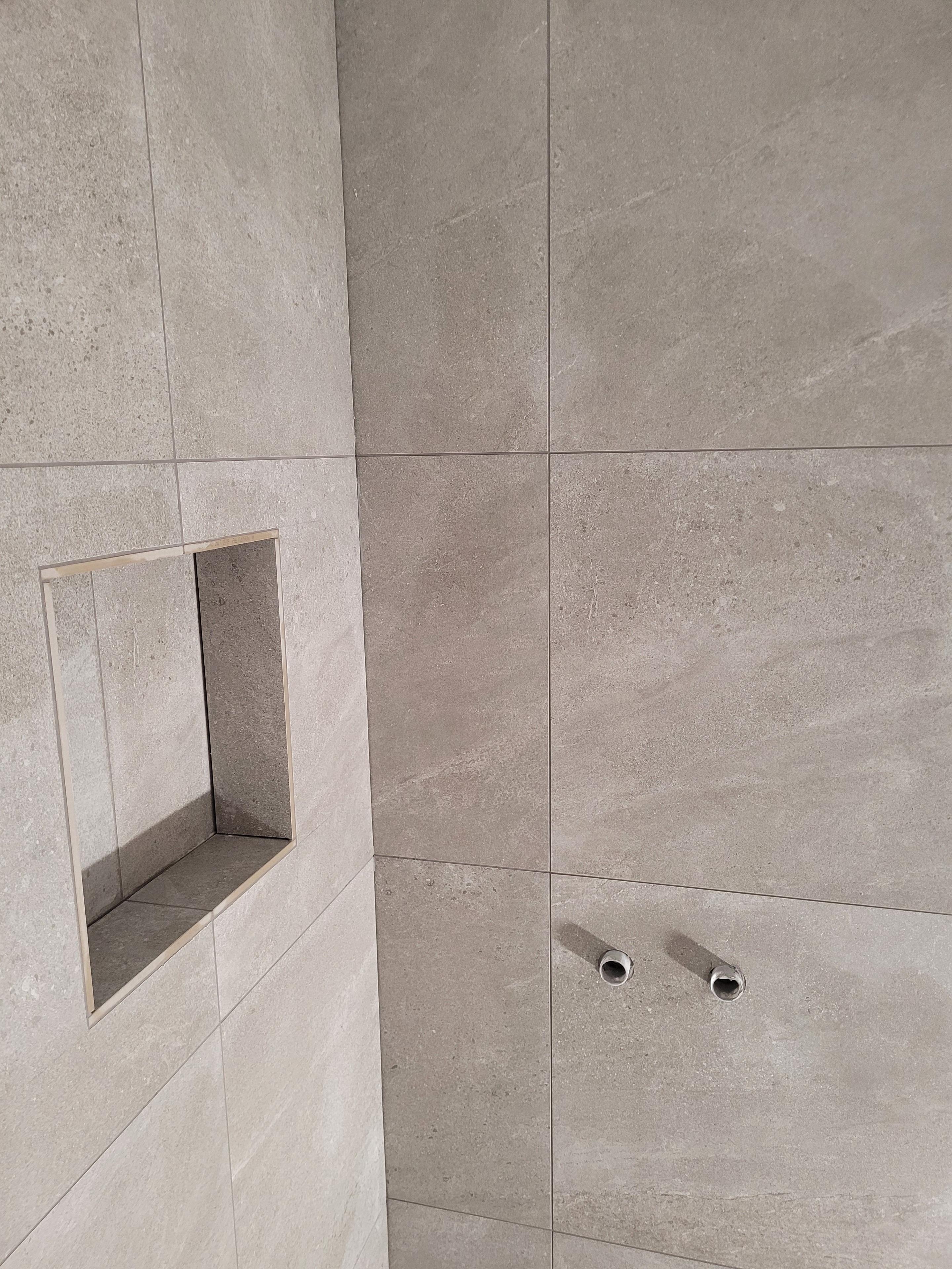 Moderne brusevæg med grå fliser og en indbygget hylde til sæbe og shampoo.