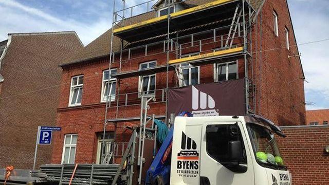 Bygning under renovering med stillads og lastbil parkeret foran.