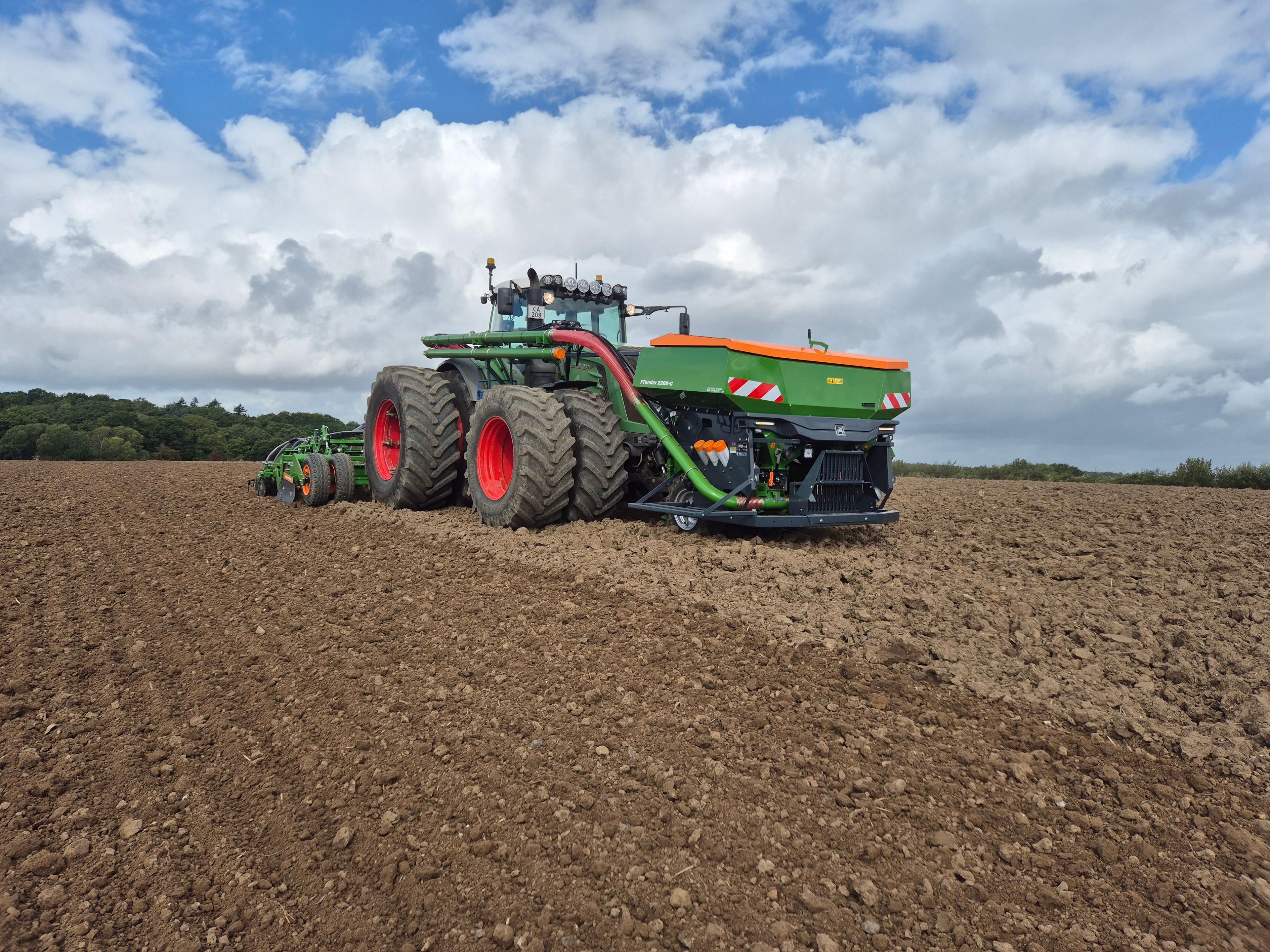 En stor traktor arbejder på en nypløjet mark under en skyet himmel.