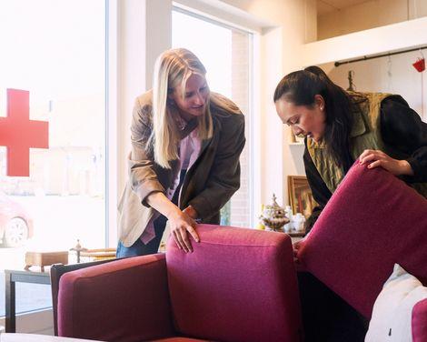 To kvinder undersøger en pink sofa i en møbelforretning.