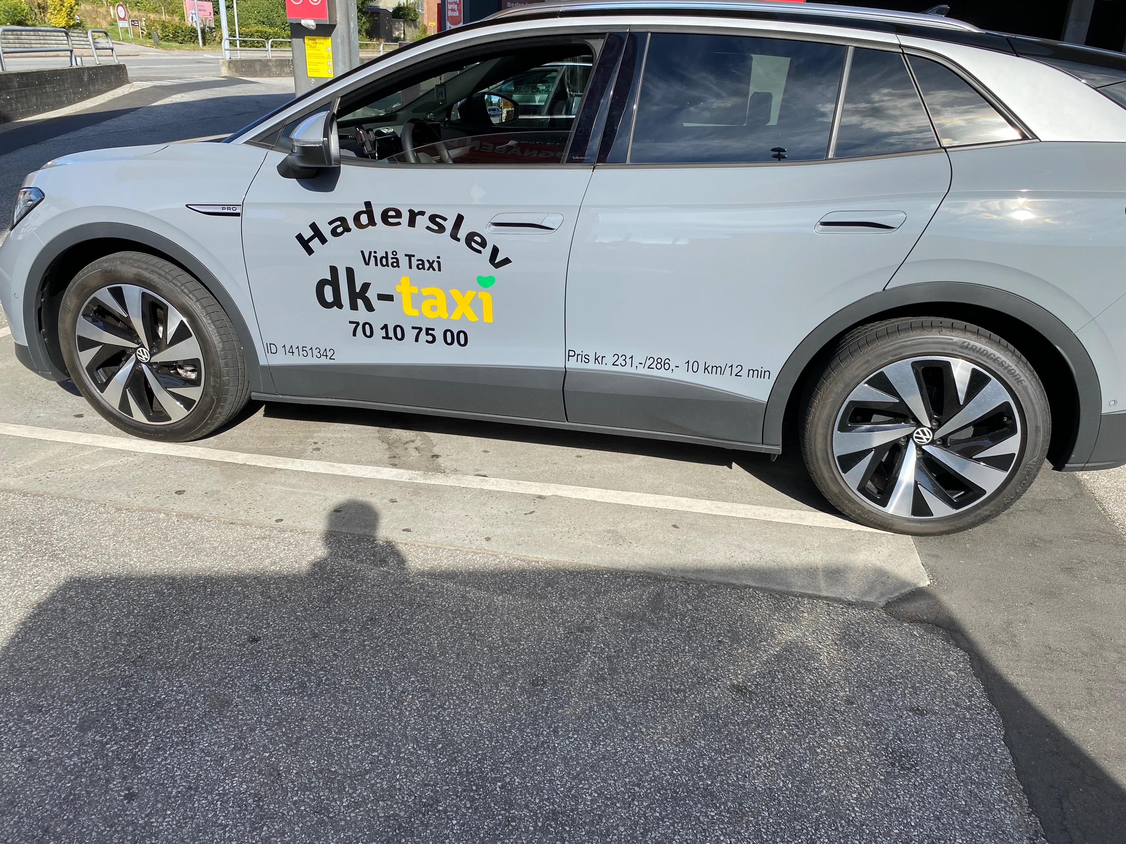 Grå taxa fra dk-taxi med teksten "Haderslev" og telefonnummeret 76 10 75 00 på siden.