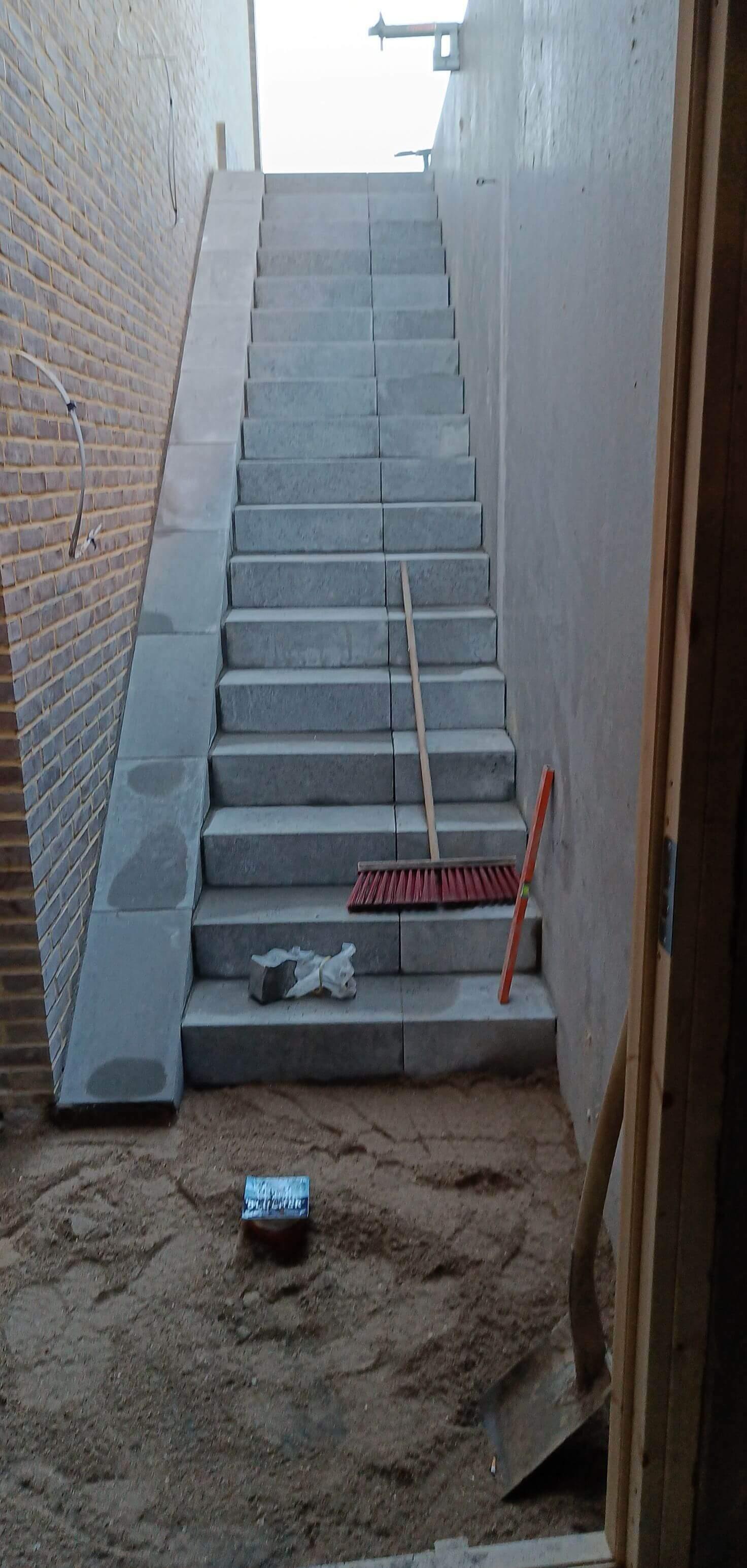 Trappe med grå fliser, der fører opad, omgivet af sand og værktøj i en byggeplads.